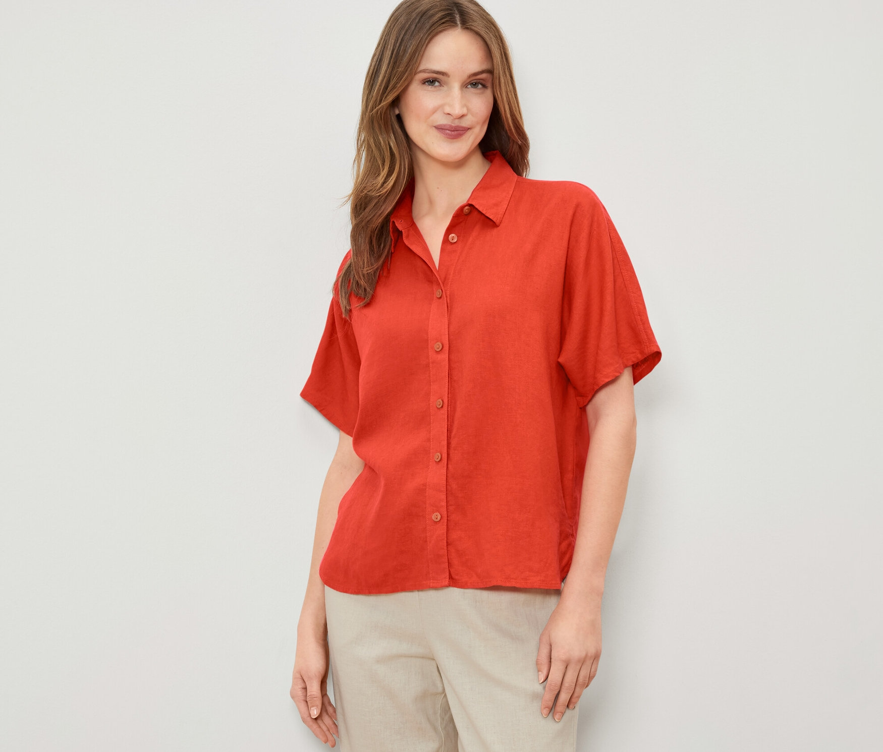 Žena má na sobě oranžovou lněnou halenku.