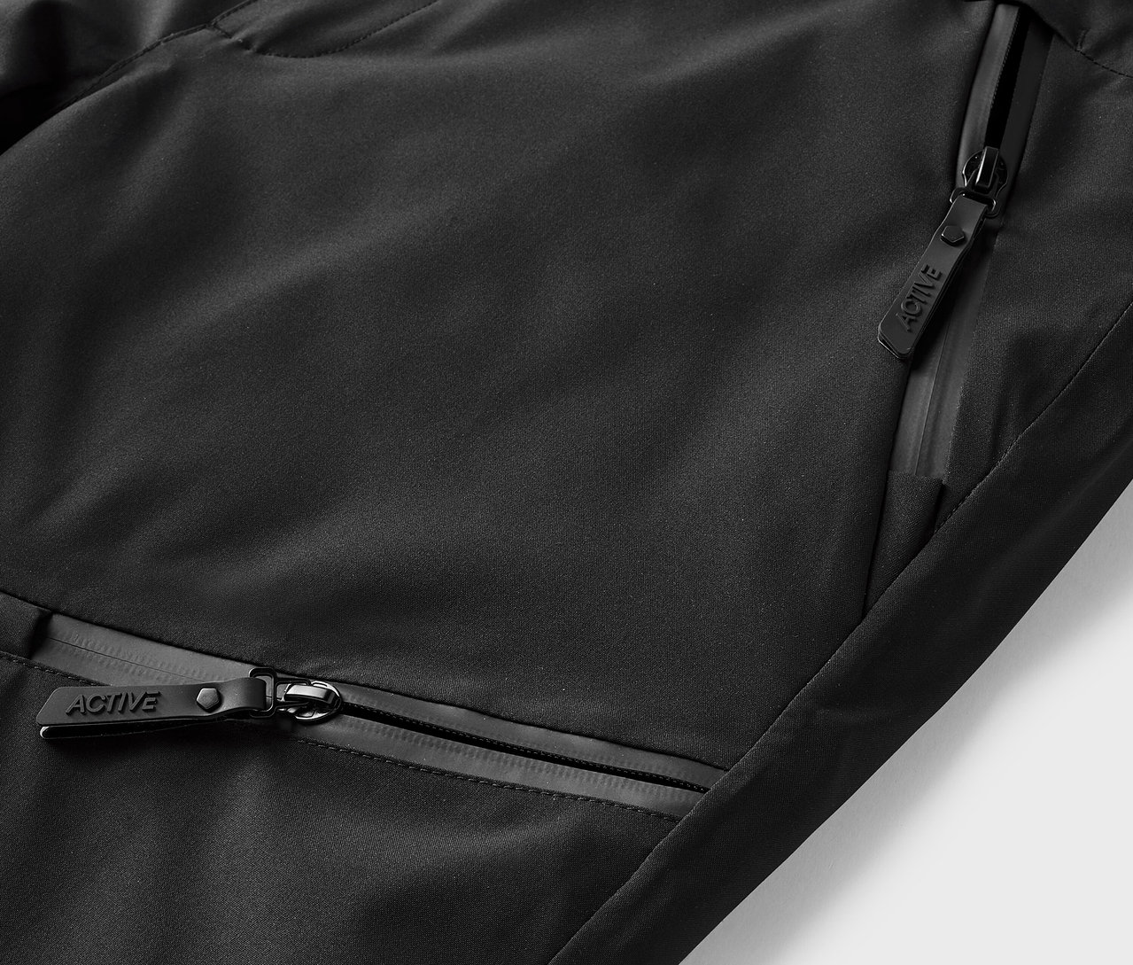 Detail černého sportovního oblečení s kapsami na zip.