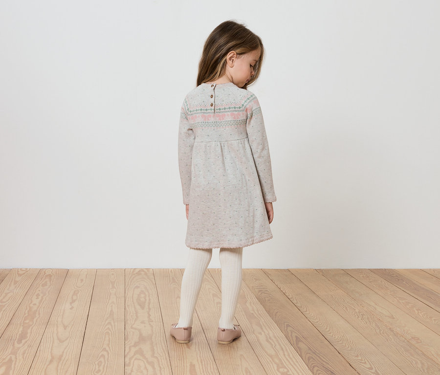 Dívka v šatech s dlouhým rukávem stojí zády ke kameře.