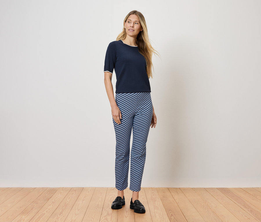 Žena stojí na dřevěné podlaze a má na sobě tmavě modré tričko a modro-bílé pruhované kalhoty.