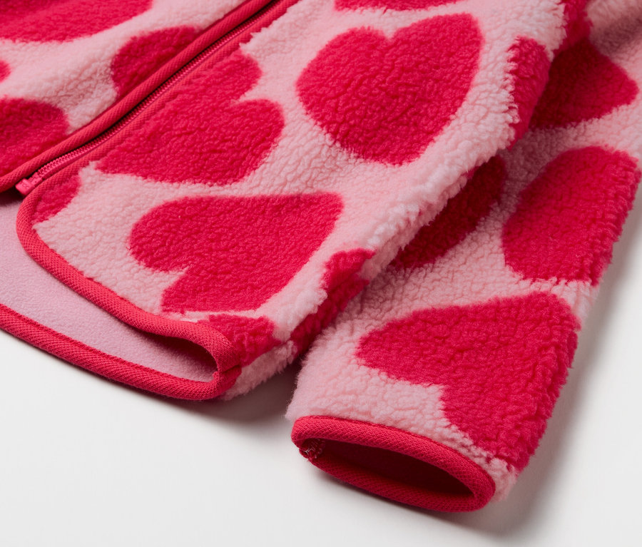 Detail růžové fleecové bundy se vzorem červených srdíček.