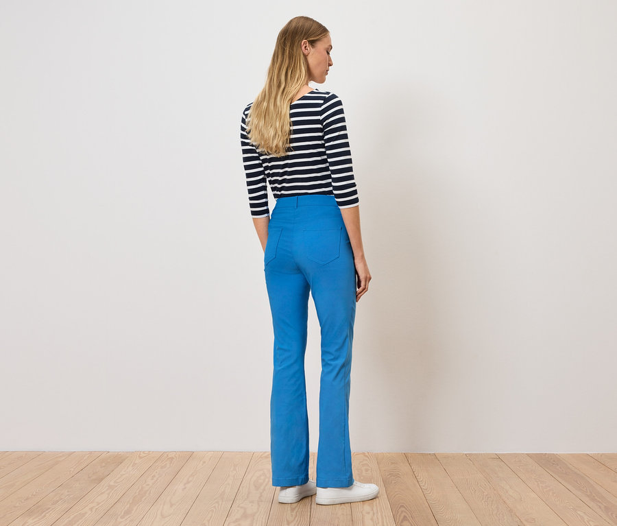 Žena stojí zády a má na sobě modré kalhoty a pruhované tričko.