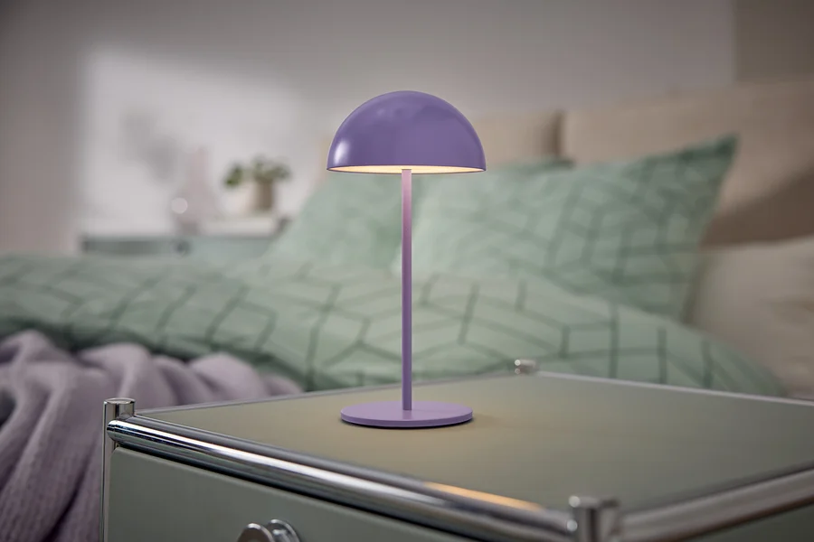 Fialová lampa stojí na nočním stolku vedle postele.