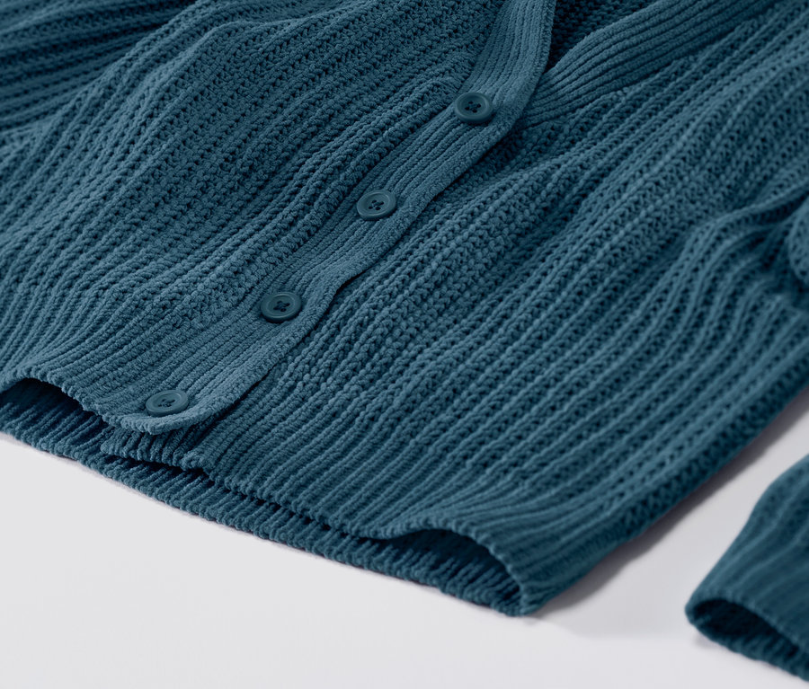 Detailní záběr na petrolejový pletený kabátek se zapínáním na knoflíky.