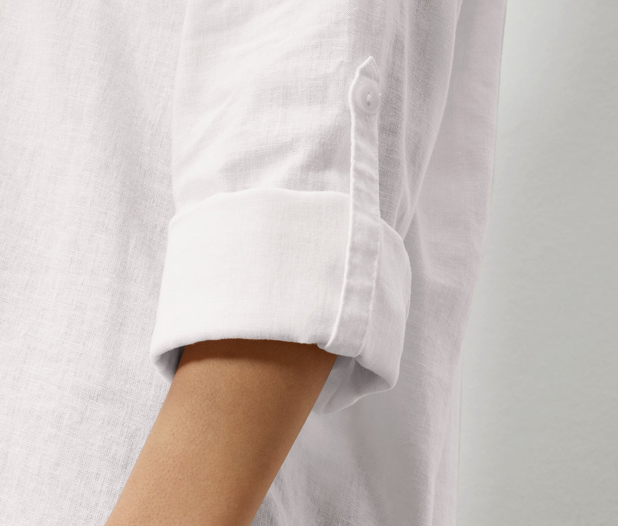 Detailní pohled na rukáv bílé lněné košile s ohrnutým rukávem a knoflíkem.