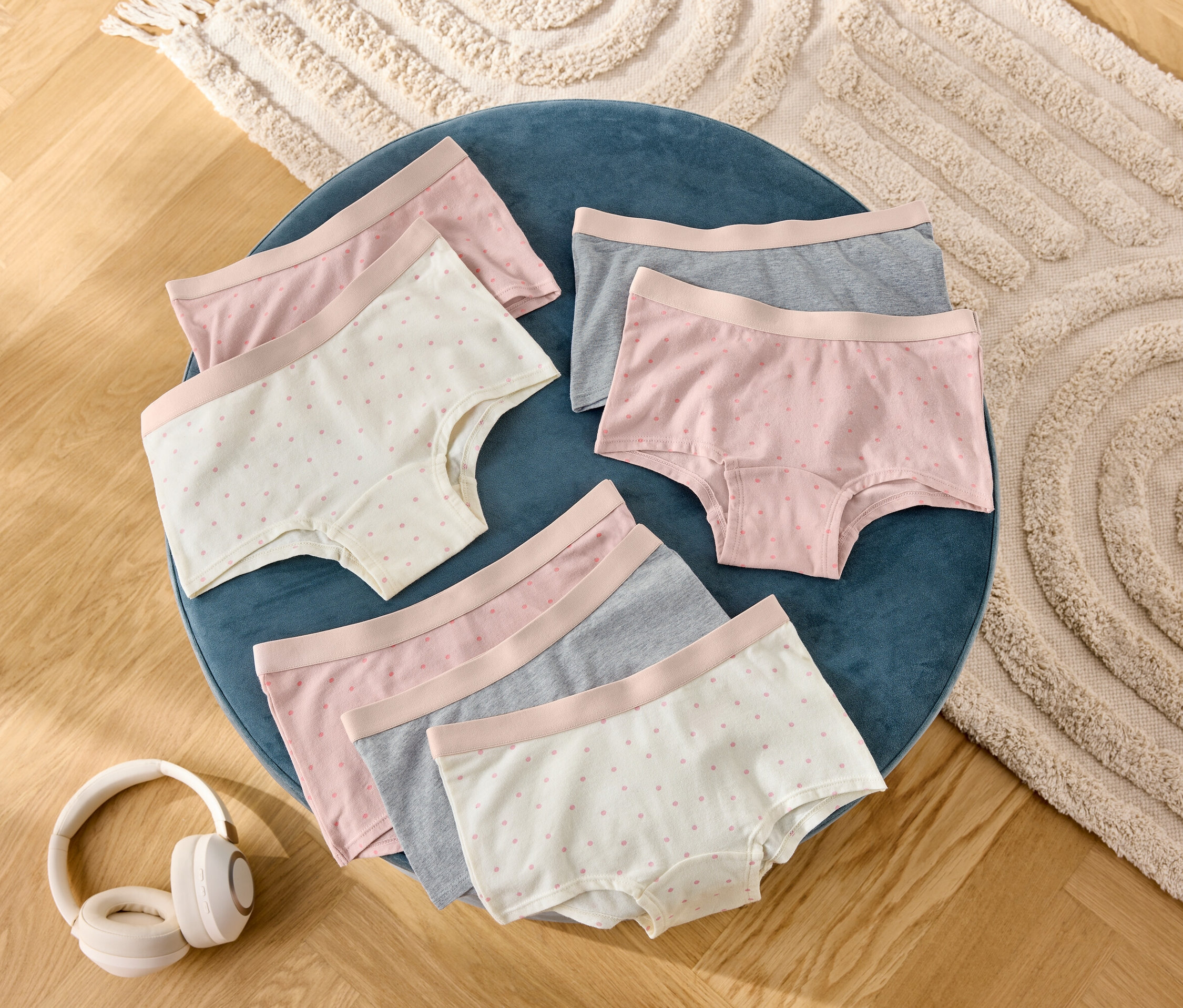Na modré stoličce leží šest párů dámských šortek v šedé, růžové a puntíkované barvě, vedle nich jsou sluchátka.