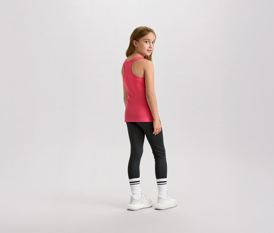 Mladá dívka se dívá přes rameno, má na sobě růžové tílko, legíny a bílé tenisky.