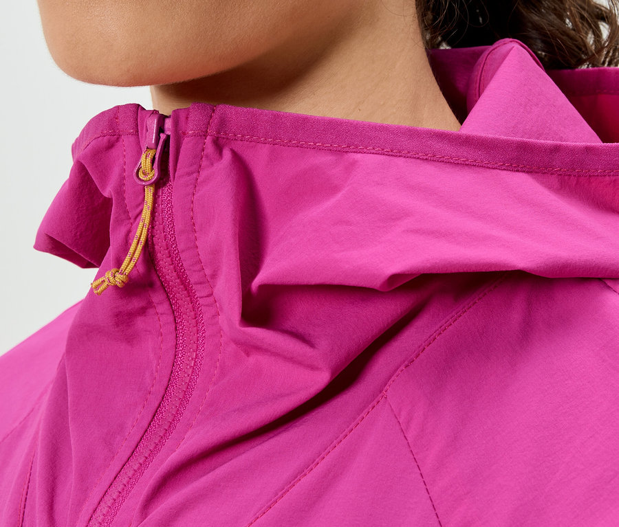 Detailní záběr ženy v růžové bundě s kapucí a žlutým zipem.