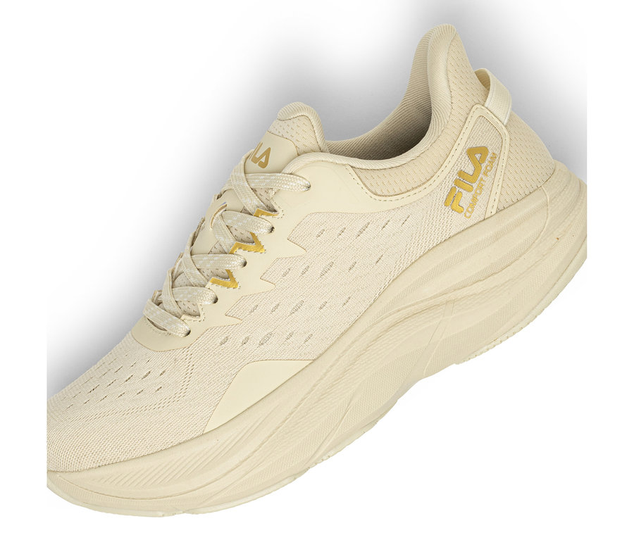 Jedna světle béžová teniska se síťovaným svrškem a silnou, texturovanou podrážkou. Na boku je viditelné zlaté logo Fila a nápis „COMFORT FOAM“. Tkaničky jsou béžové se zlatými akcenty.