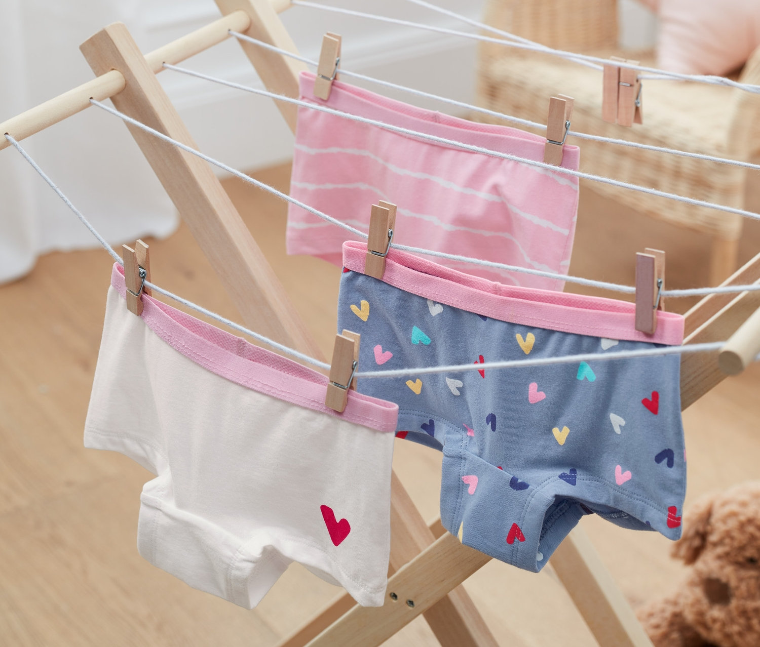 Tři dívčí kalhotky z biobavlny visí na dřevěném sušáku s kolíčky.