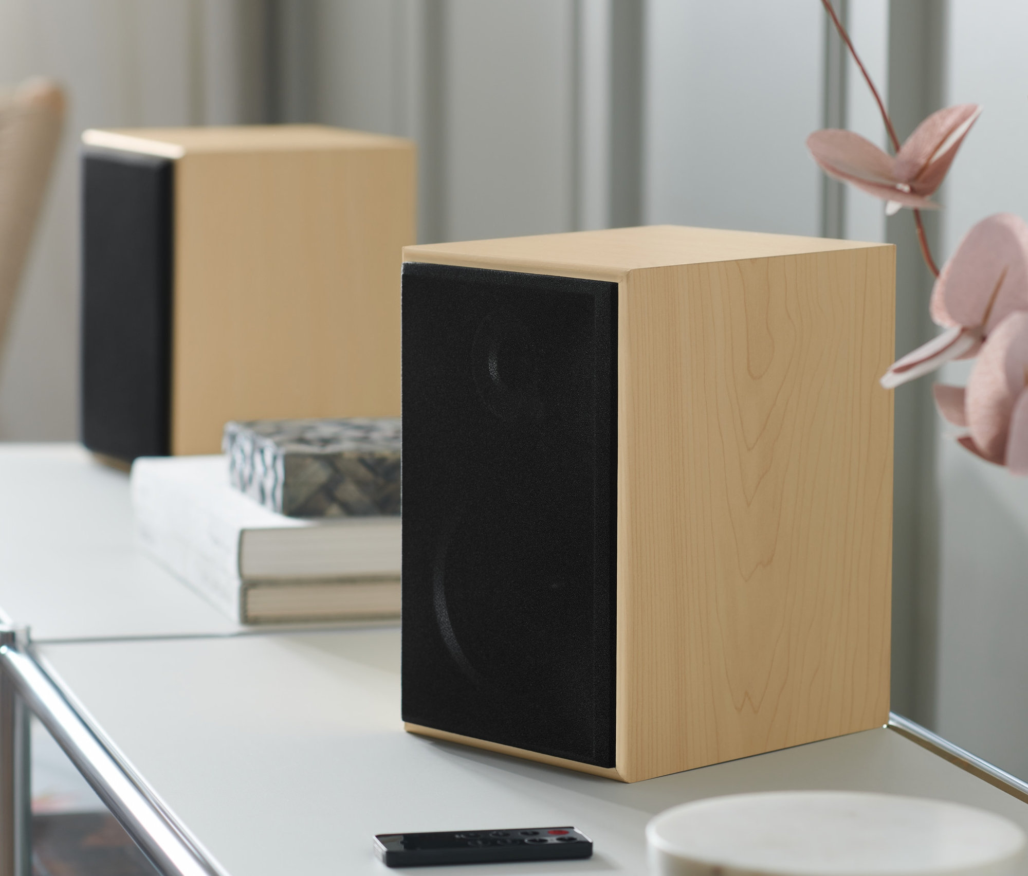 Dva stereo reproduktory s Bluetooth® na bílém stolku s dálkovým ovládáním.