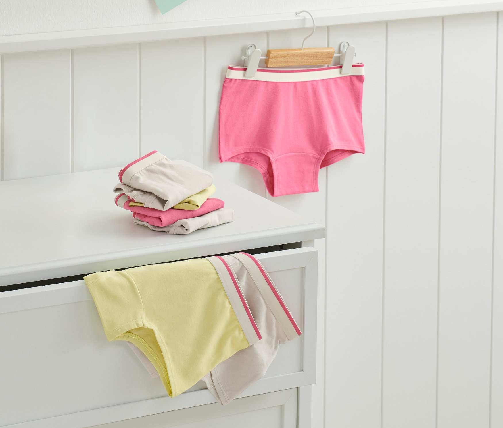 Na komodě leží složených 7 dívek v růžové barvě a jedny visí na ramínku.