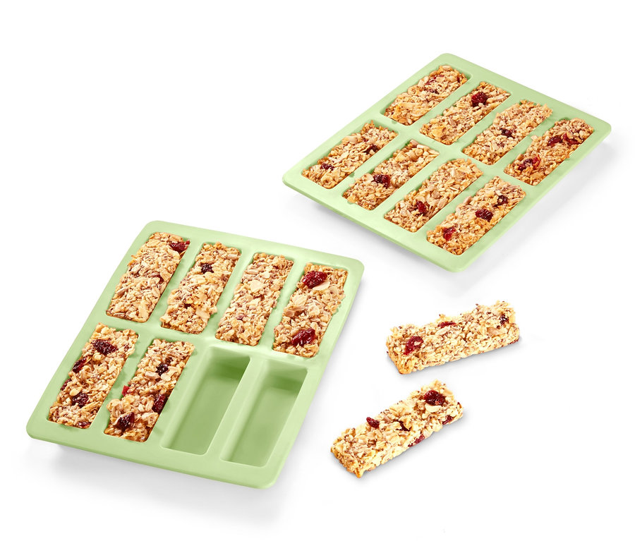 Dvě zelené formy na müsli tyčinky, ve kterých jsou müsli tyčinky. Dvě tyčinky leží mimo formy.