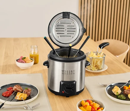 Mini fritéza a fondue na stole s jídlem na talířích a v miskách.