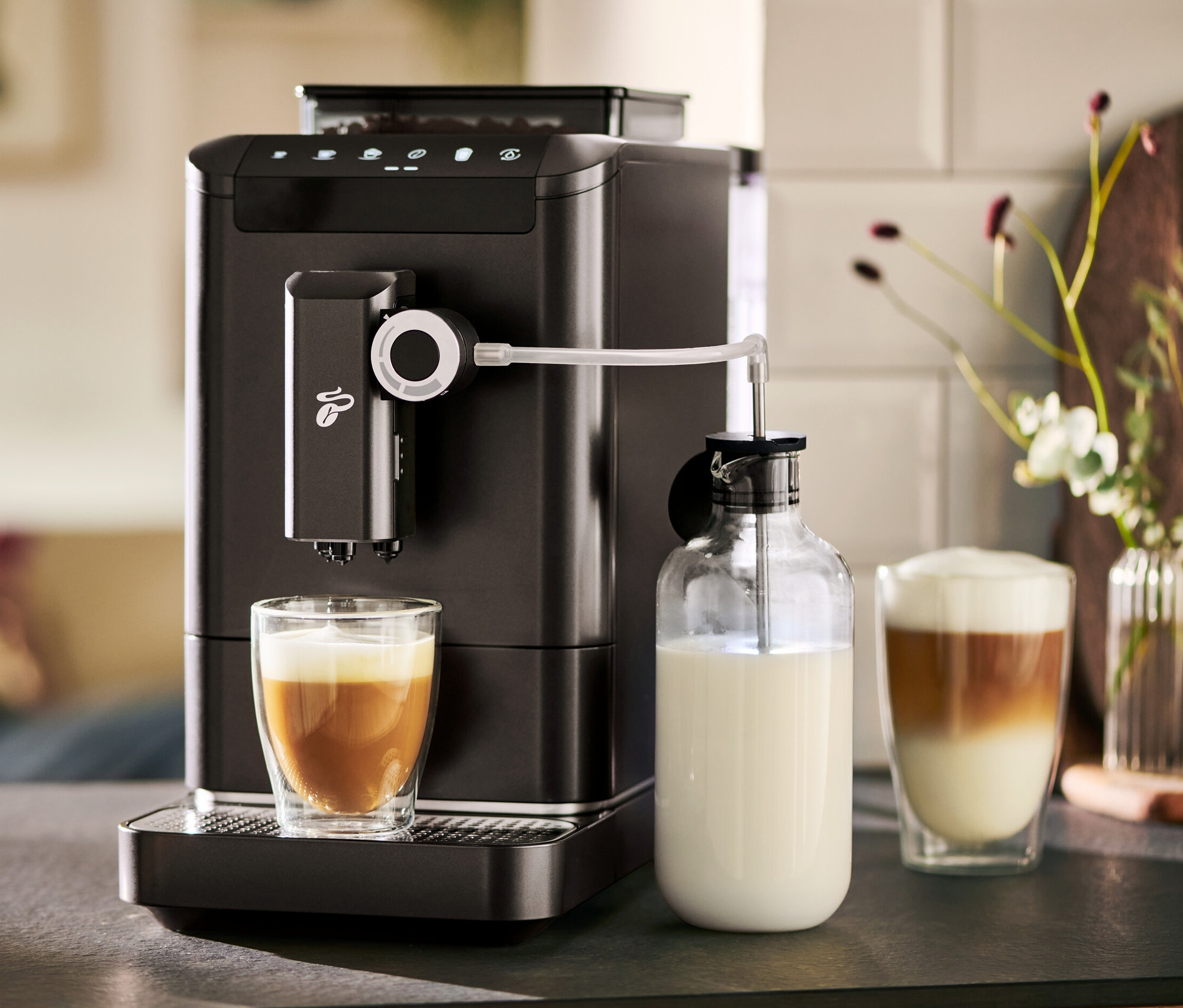 Automatický kávovar »Esperto 2 Milk« Granite Black připravuje kávu do sklenice. Vedle stojí karafa na mléko.