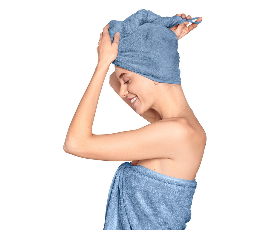 Žena si upravuje ručníkový turban na hlavě, tělo má ovinuté ručníkem.