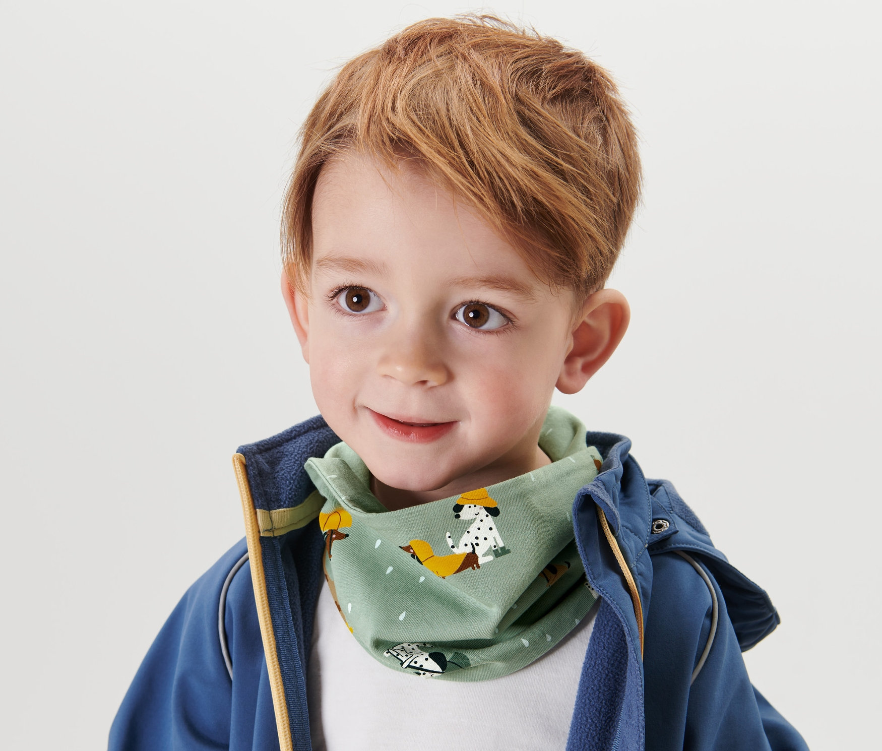 Chlapeček s hnědými vlasy a dětským šátkem na krk se suchým zipem.