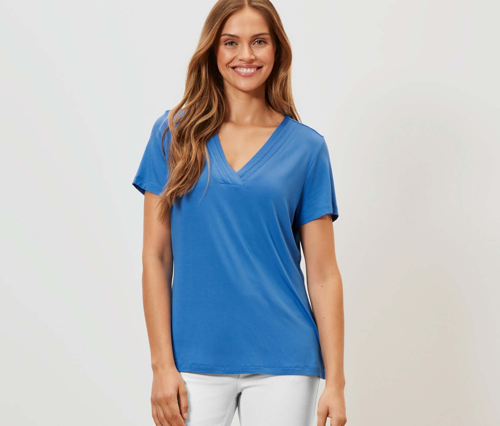 Žena má na sobě kobaltově modré tričko s detaily skladů a bílé kalhoty.