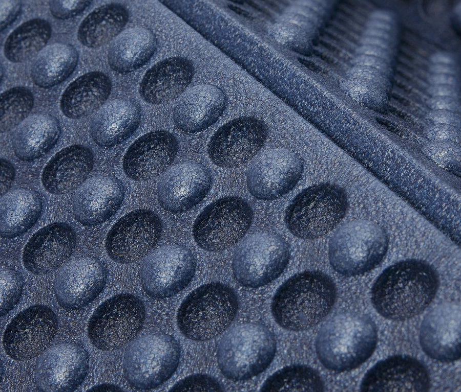 Detailní záběr na skládací karimatku modré barvy s kruhovými prohlubněmi a drážkami.