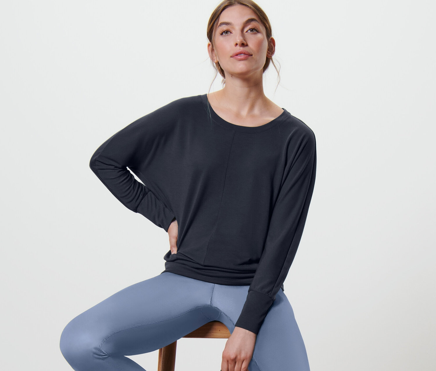 Žena sedí na stoličce a má na sobě námořnické modré sportovní triko na jógu.