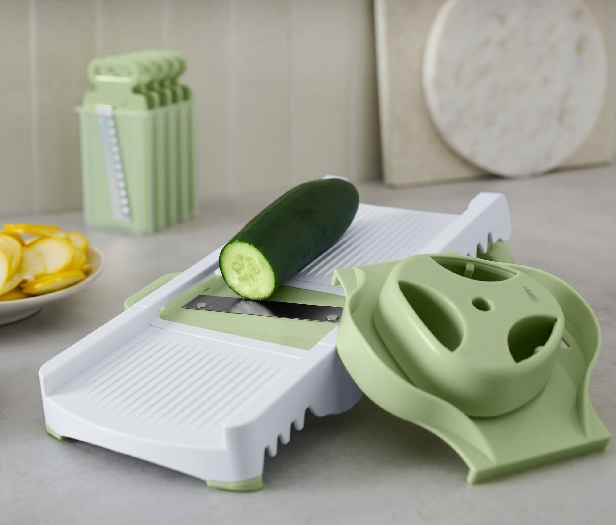 Okurka leží na multifunkčním struhadle. Vedle jsou nakrájené okurky a cukety.