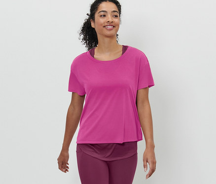 Žena kráčí a má na sobě růžové sportovní tričko s krátkým rukávem 2 v 1.