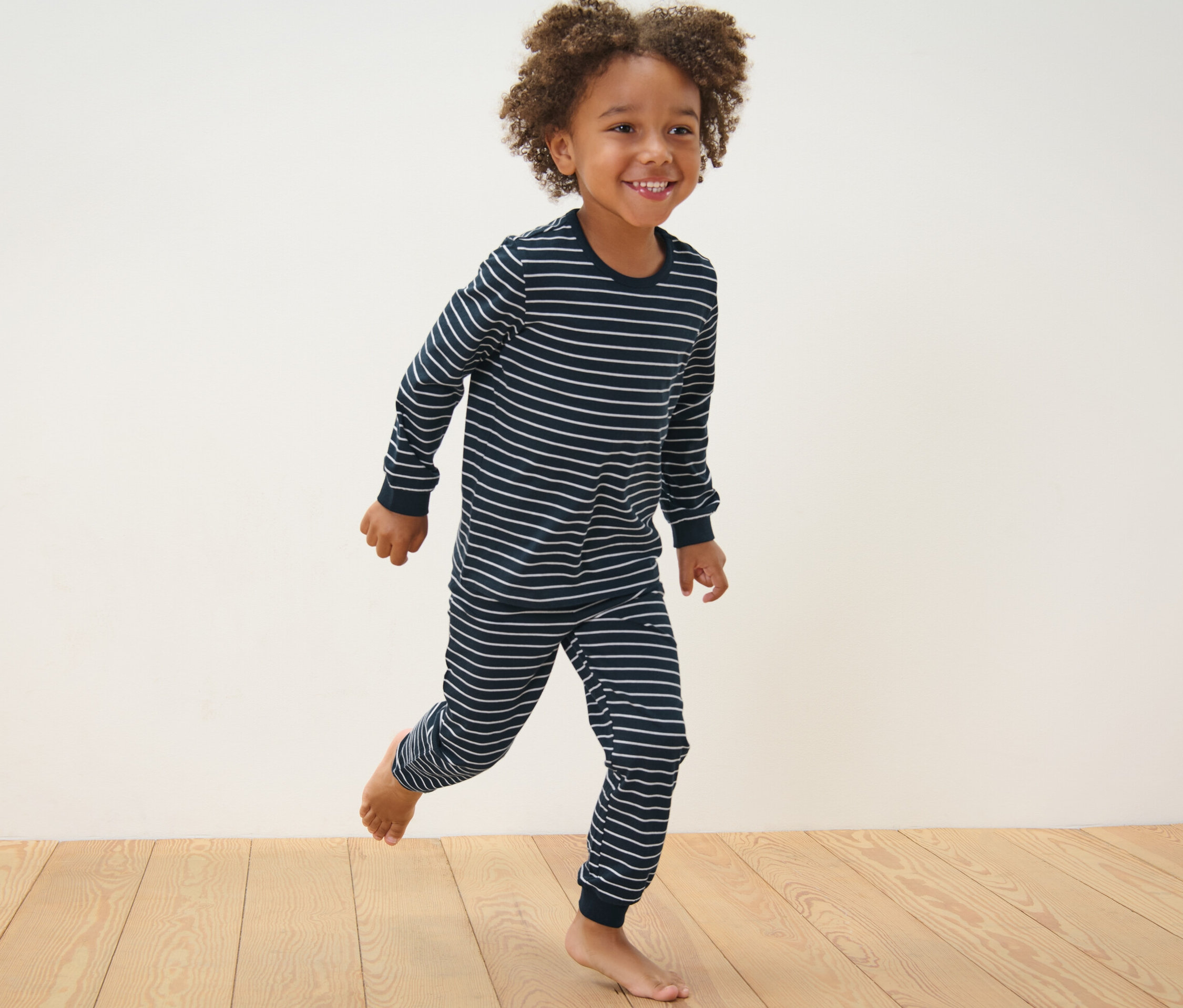 Chlapec v modrém pyžamu s proužky běží po dřevěné podlaze. Dětská pyžama, 2 ks, modrá.