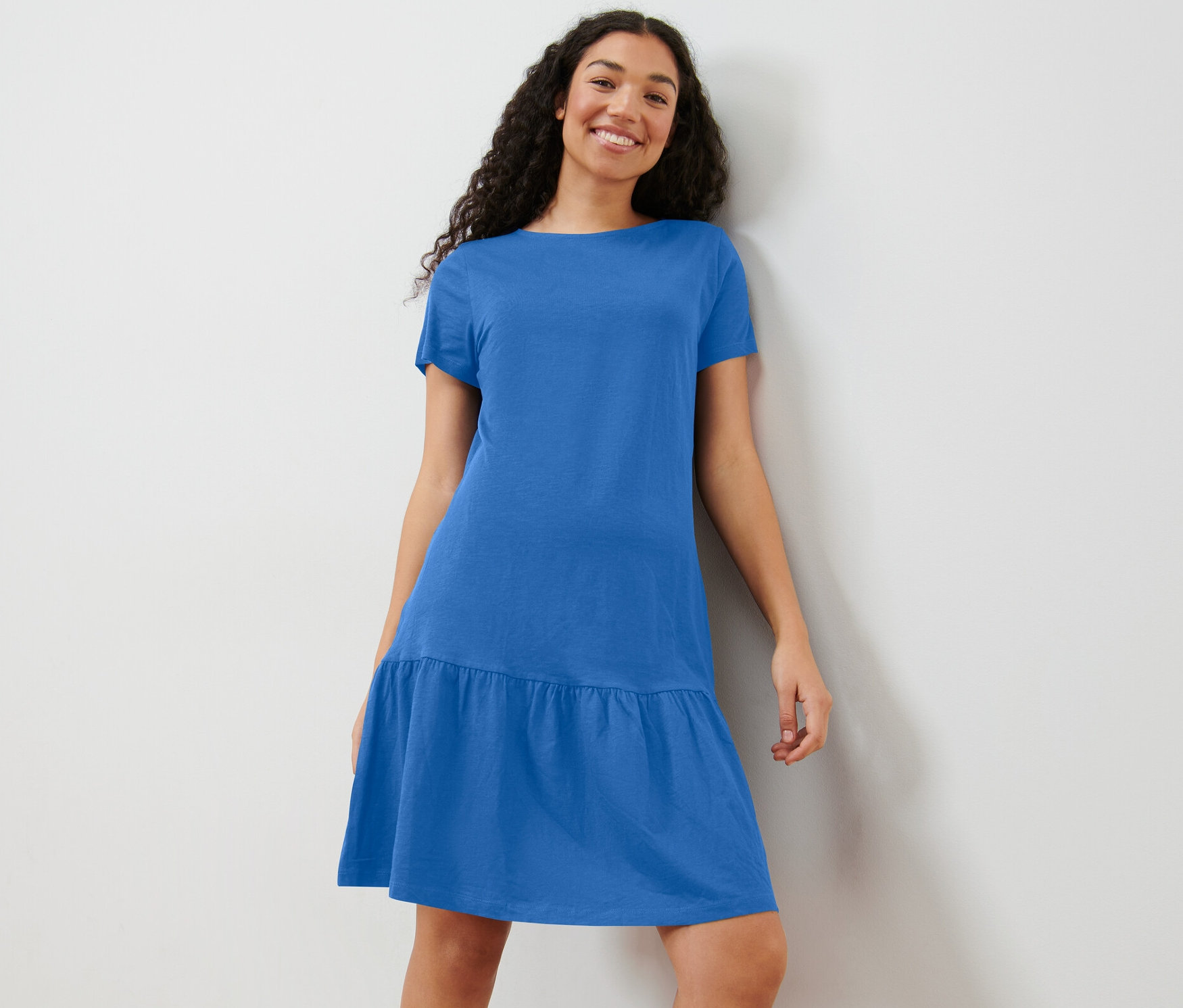 Žena pózuje v kobaltově modrých žerzejových šatech s volánem.