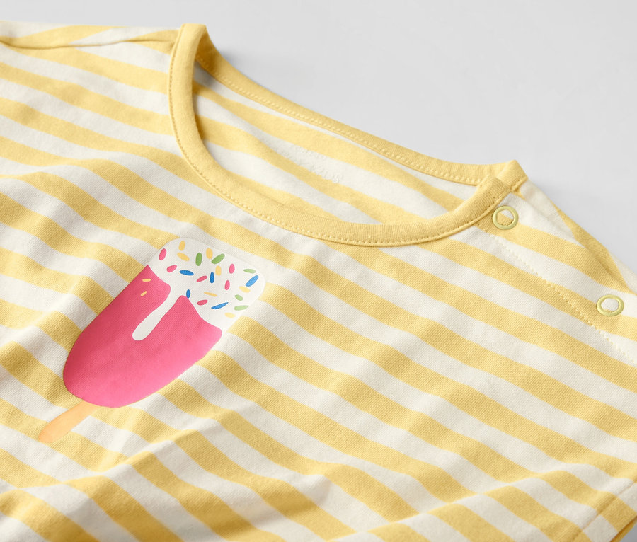 Detail dětského overalu se žlutými a bílými pruhy a potiskem nanuku.