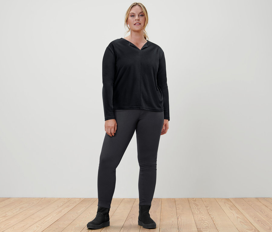 Žena stojí a má na sobě černé halenkové triko a džegíny.