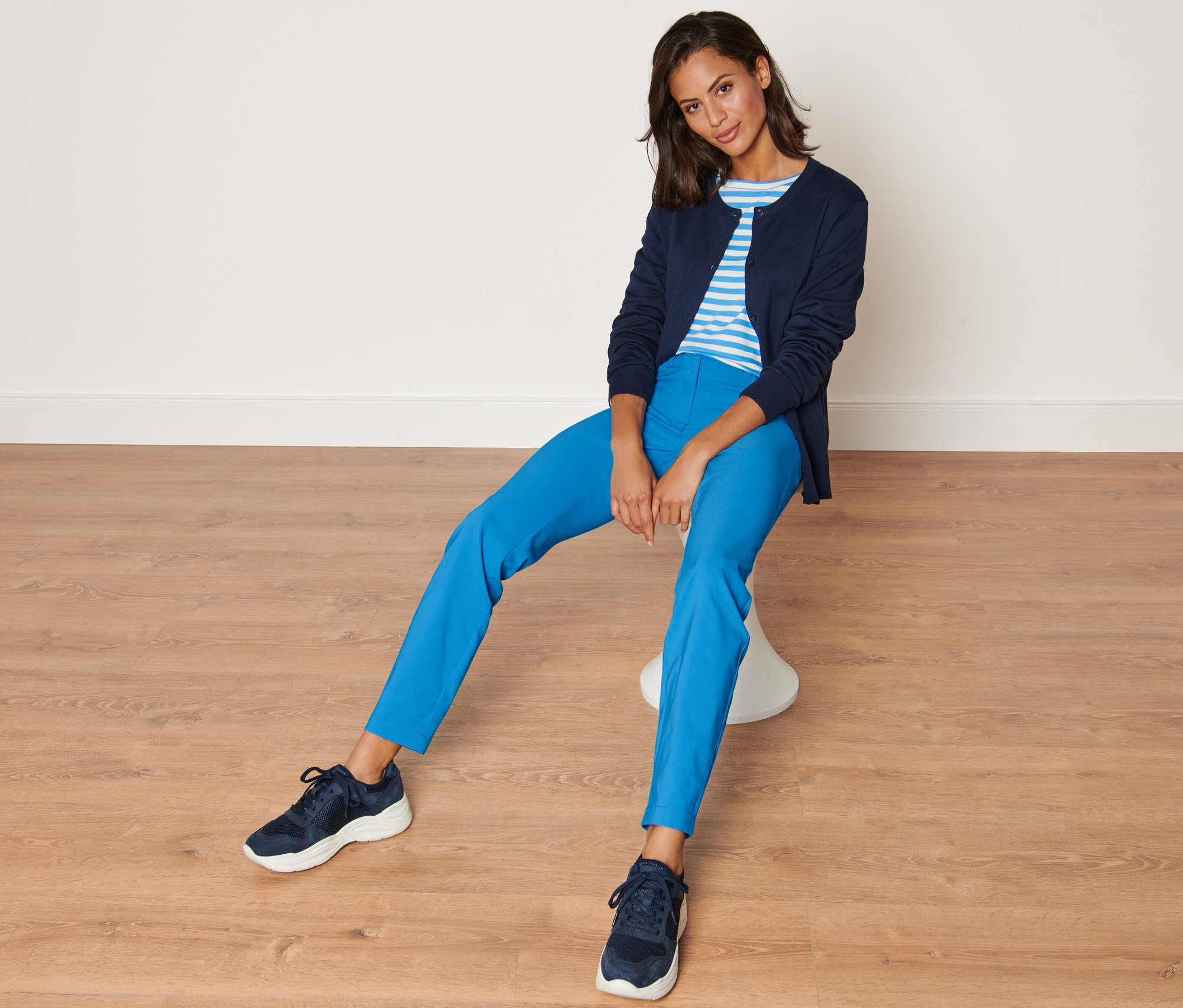 Žena sedí na stoličce a má na sobě modré bengalinové kalhoty.