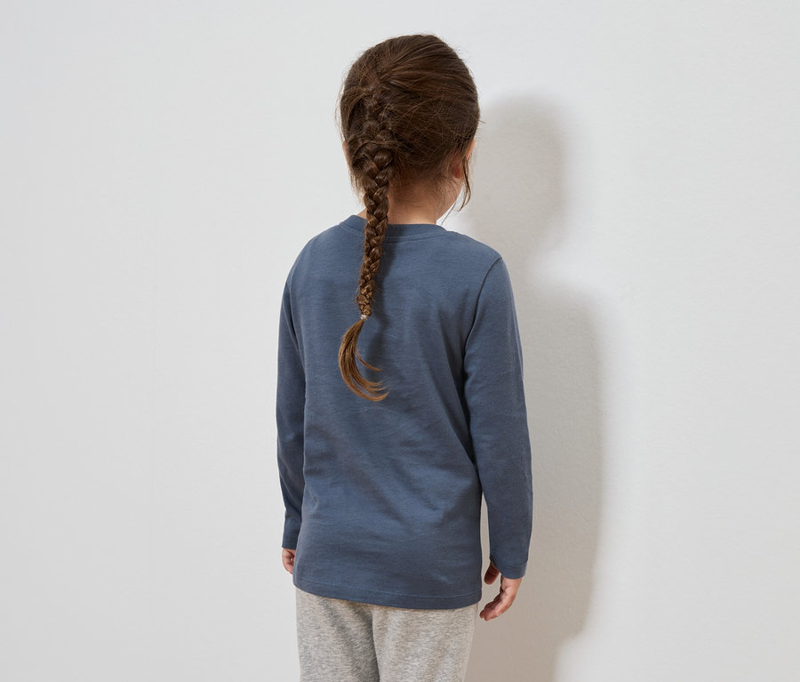 Zezadu je vidět dívka s hnědými vlasy spletenými do copu. Má na sobě modré tričko s dlouhým rukávem a šedé tepláky.