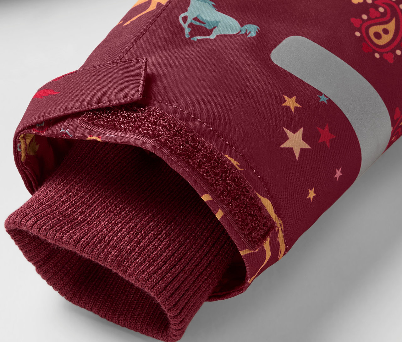 Detail bordó rukávu bundy s potiskem koní a hvězd, zakončeného bordó lemem.