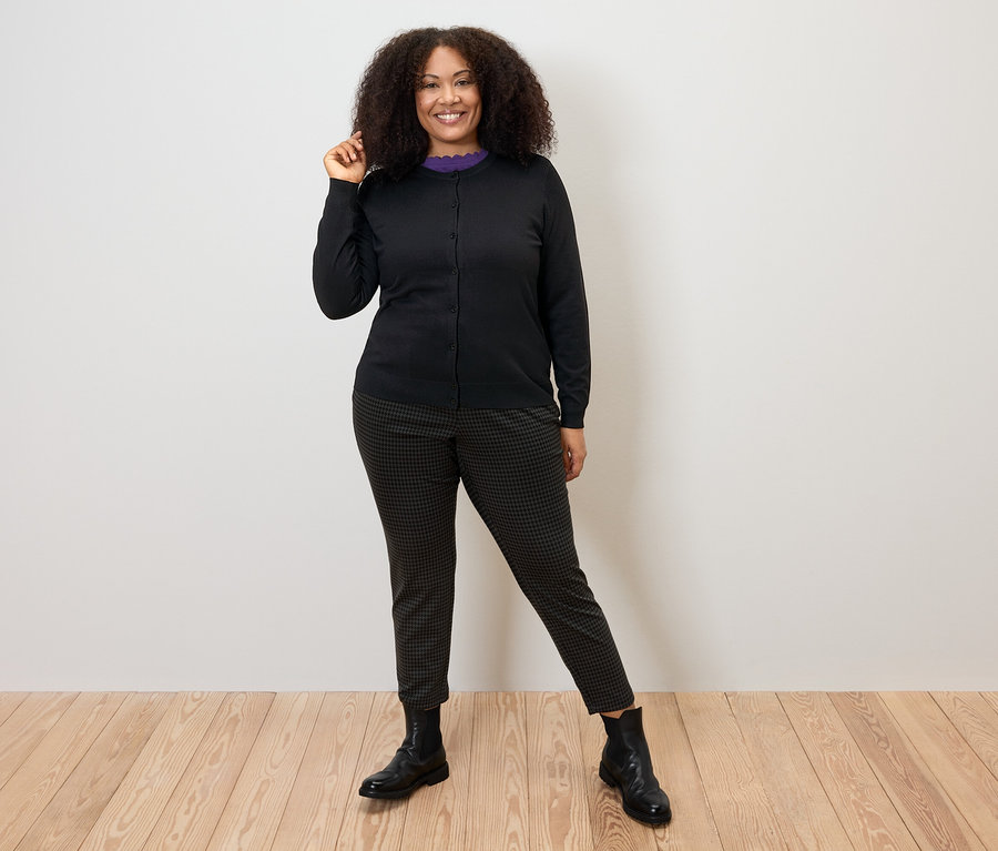 Žena pózuje v černém svetru z jemného úpletu, kalhotách a botách.