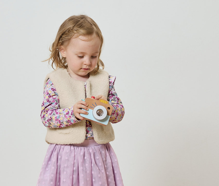 Holčička s blond copánky drží hračkový fotoaparát.