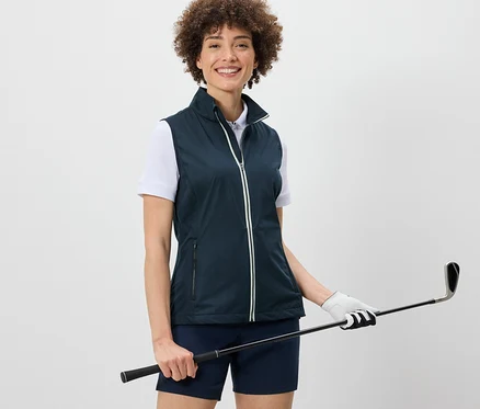 Žena má na sobě softshellovou vestu a drží golfovou hůl.