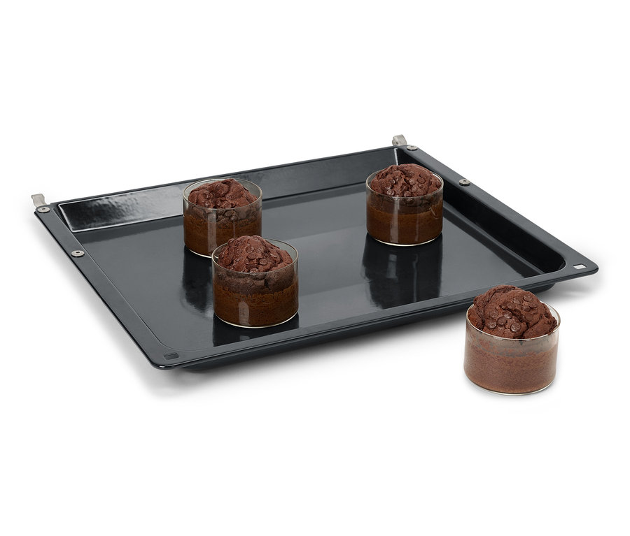 Čtyři čokoládové muffiny ve sklenicích na černém plechu na pečení.