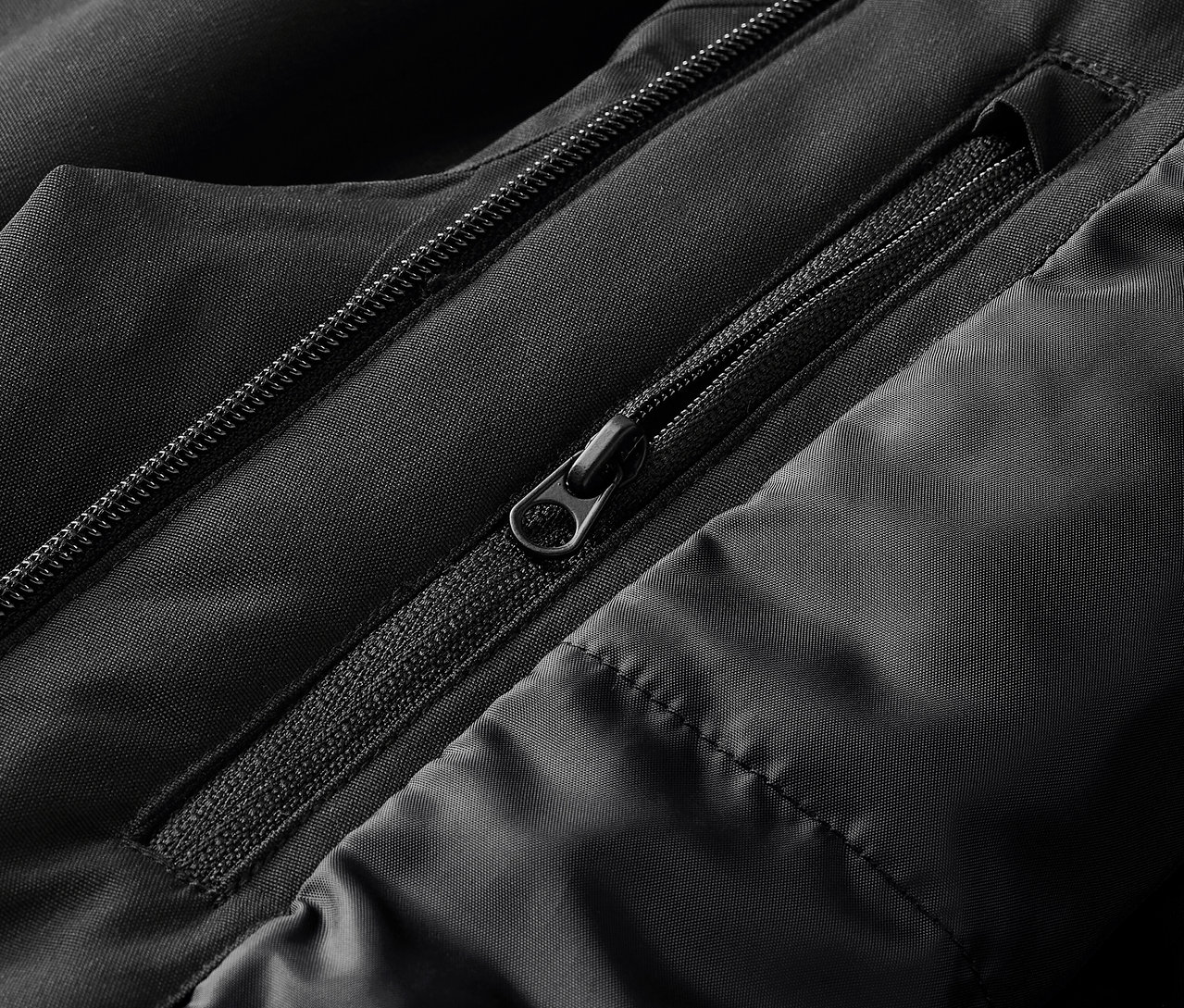 Detail černé bundy s viditelnými zipy a prošíváním.