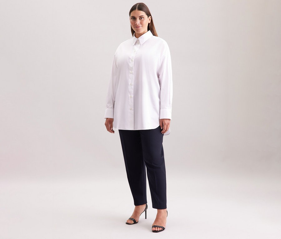 Žena má na sobě bílou dlouhou halenku oversize Seidensticker, tmavé kalhoty a černé sandály.