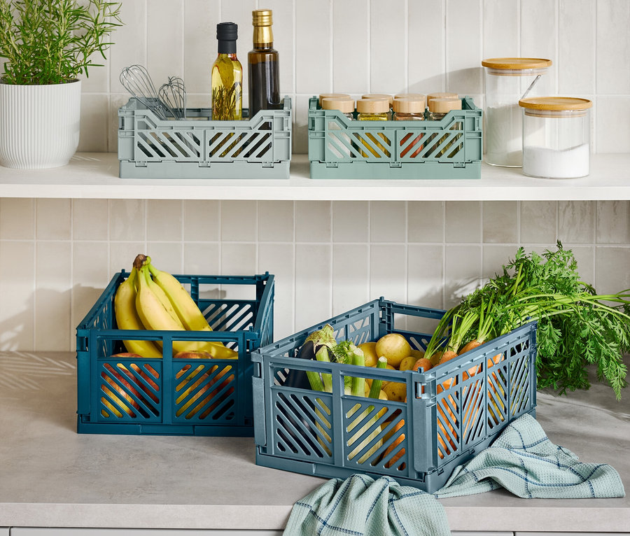 Na lince jsou tři skládací přepravky, jedna modrá s banány, jedna šedá se zeleninou a jedna šedá s kuchyňskými potřebami.