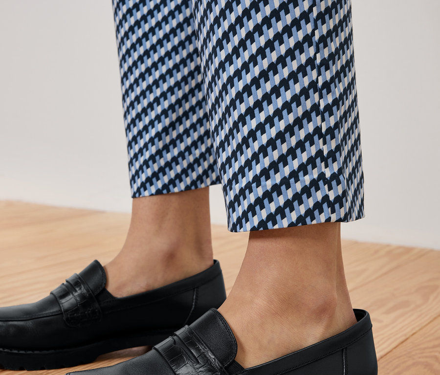 Nohavice s modrobílým vzorem a černé kožené mokasíny na dřevěné podlaze.