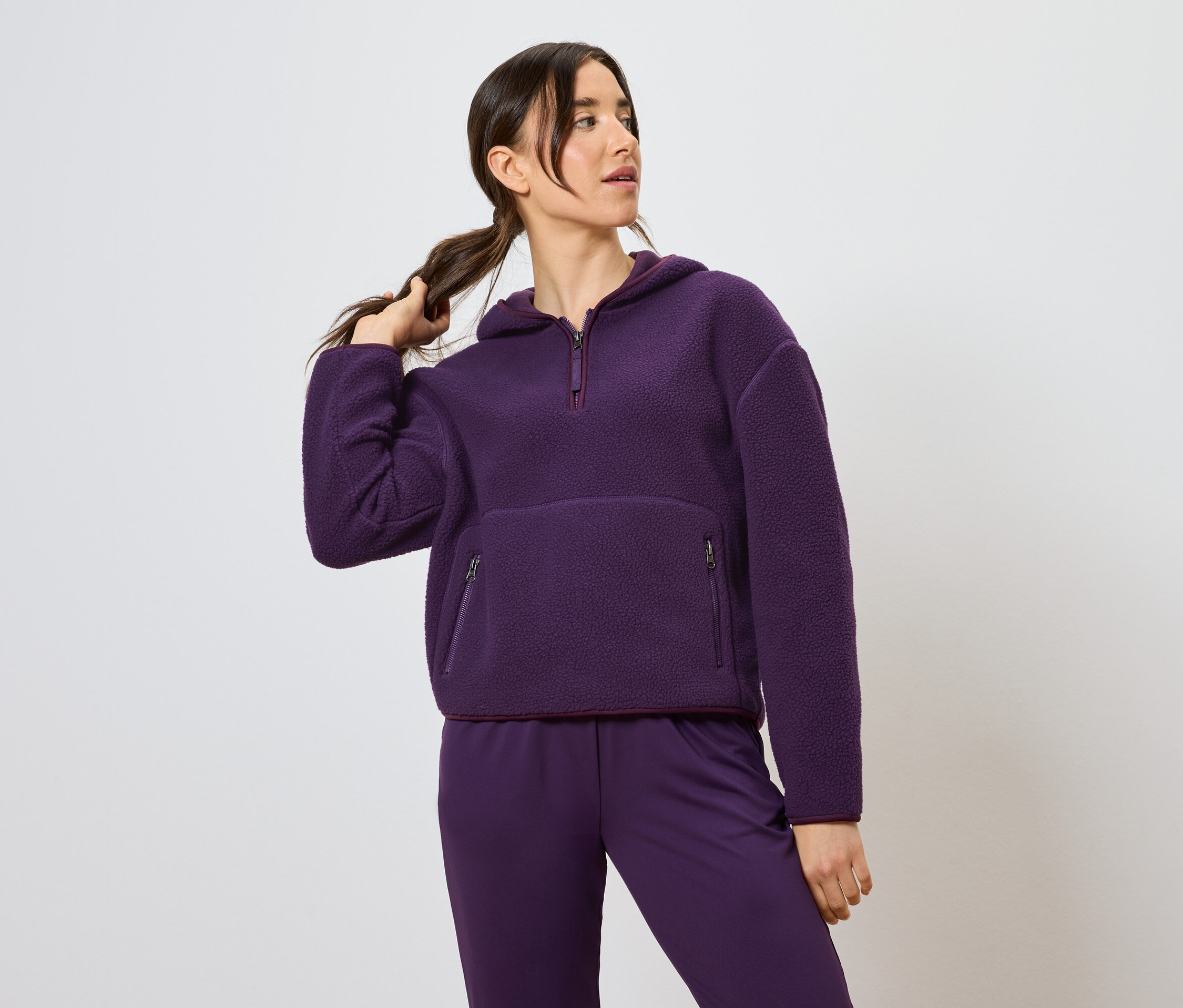Žena drží culík, oblečená do fialové mikiny s kapucí a kalhot.