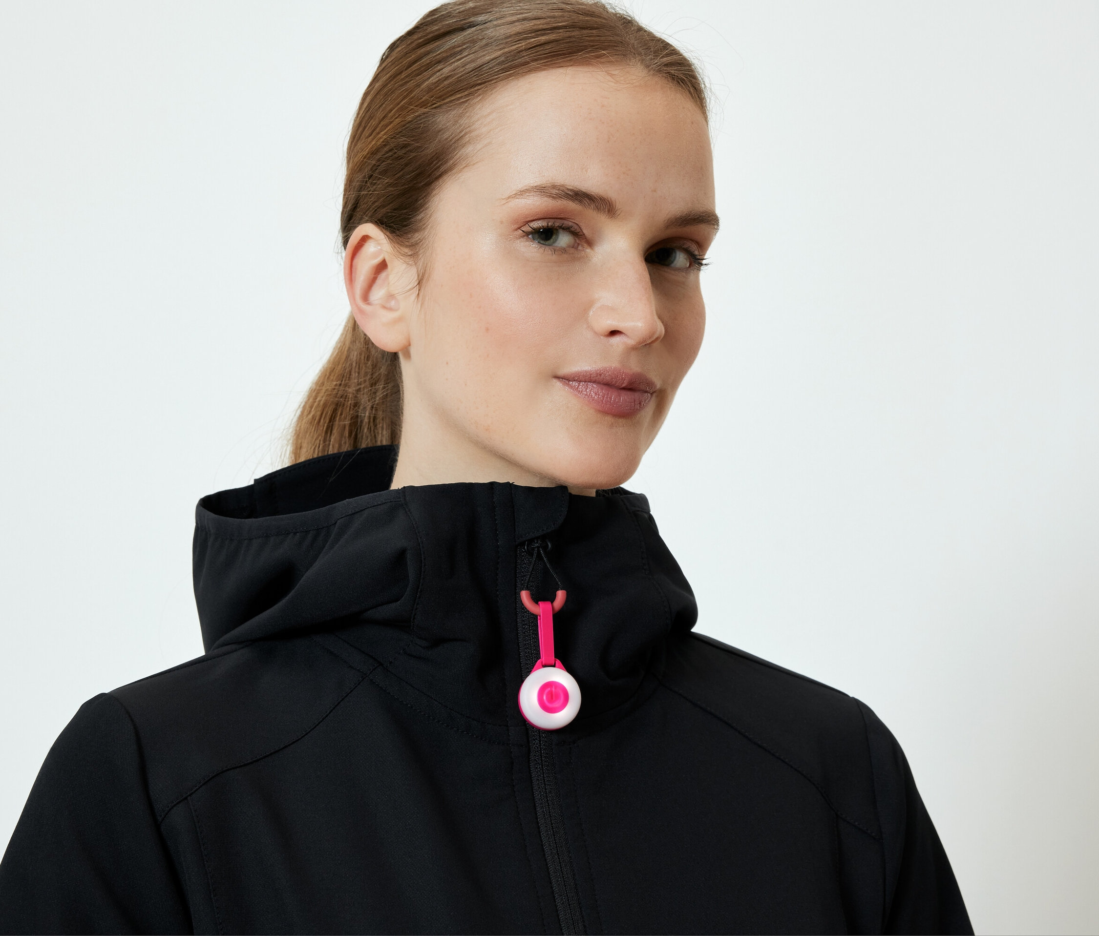 Žena má na sobě černou bundu s kapucí a růžovým zipem.