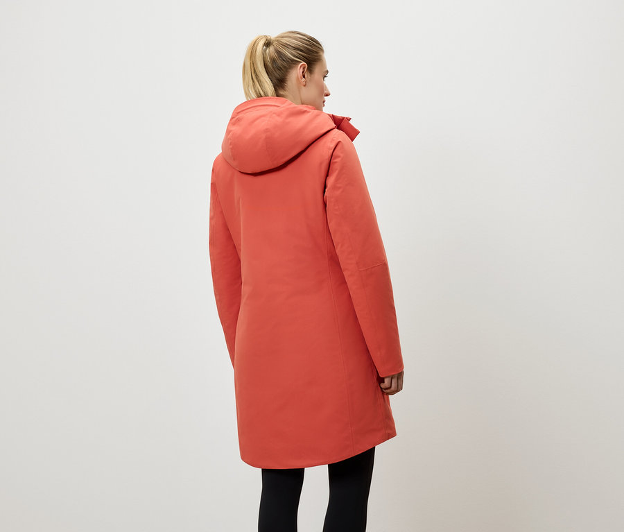 Žena zády k fotoaparátu má na sobě korálově červený kabát s kapucí a černé legíny.
