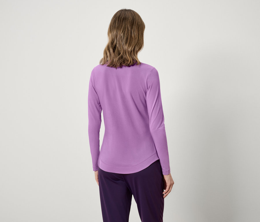 Zezadu pohled na ženu s vlnitými vlasy v levandulovém topu s dlouhým rukávem a fialových kalhotách.