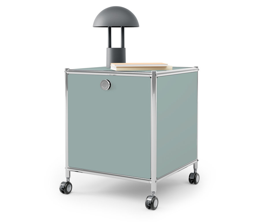 Šedá lampa a kniha na modrozeleném úložném boxu na kolečkách.