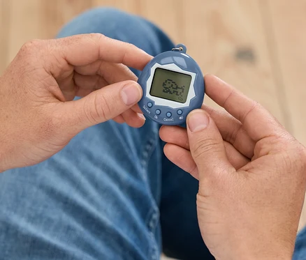 Muž drží v rukou modré Tamagotchi.