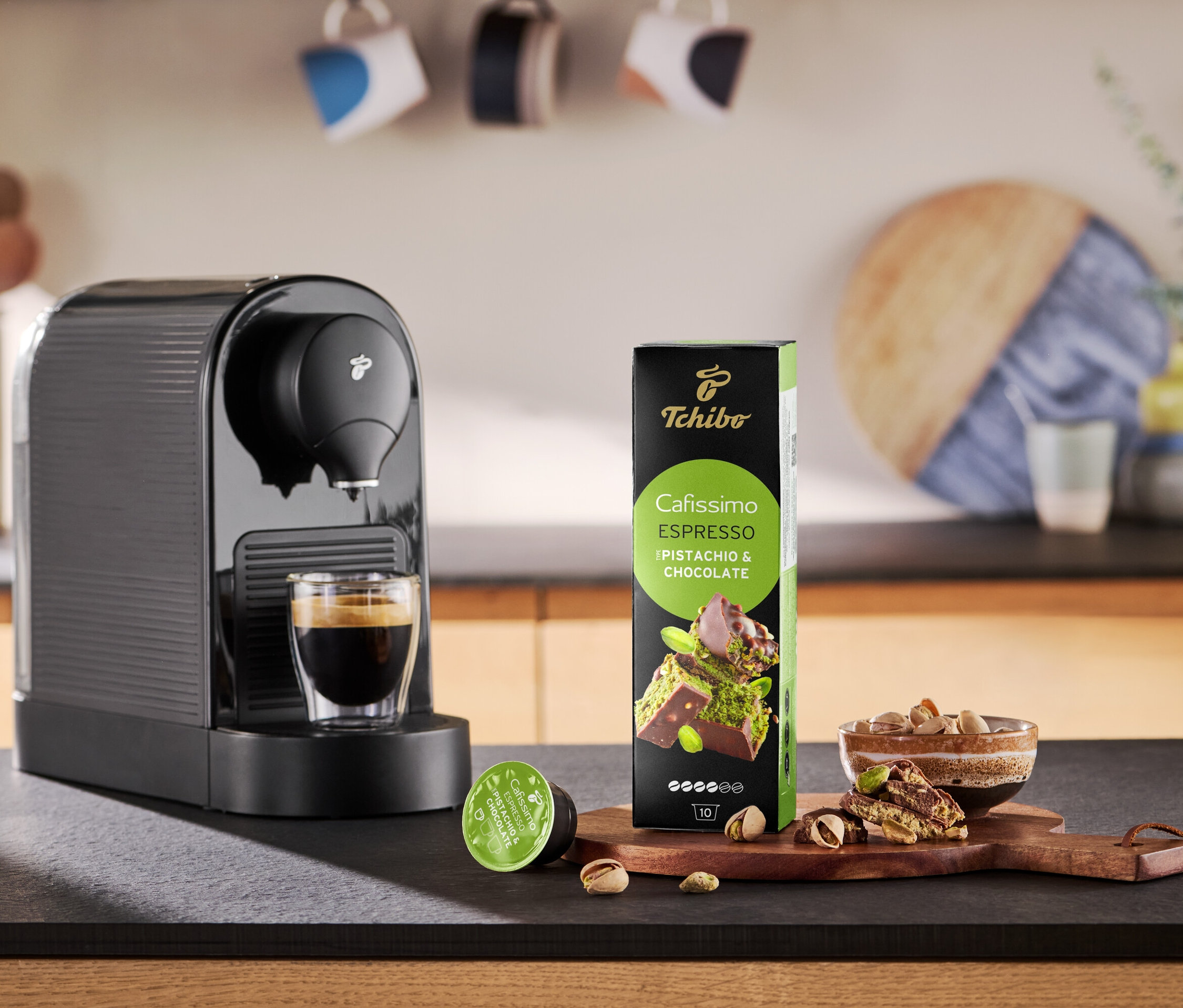 Kávovar nalévá kávu do šálku vedle balení kapslí Cafissimo Flavoured Espresso.