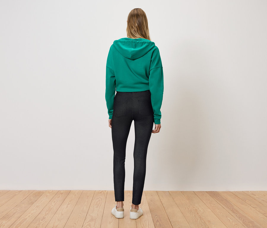Žena stojí zády a má na sobě zelenou mikinu s kapucí a černé legíny.