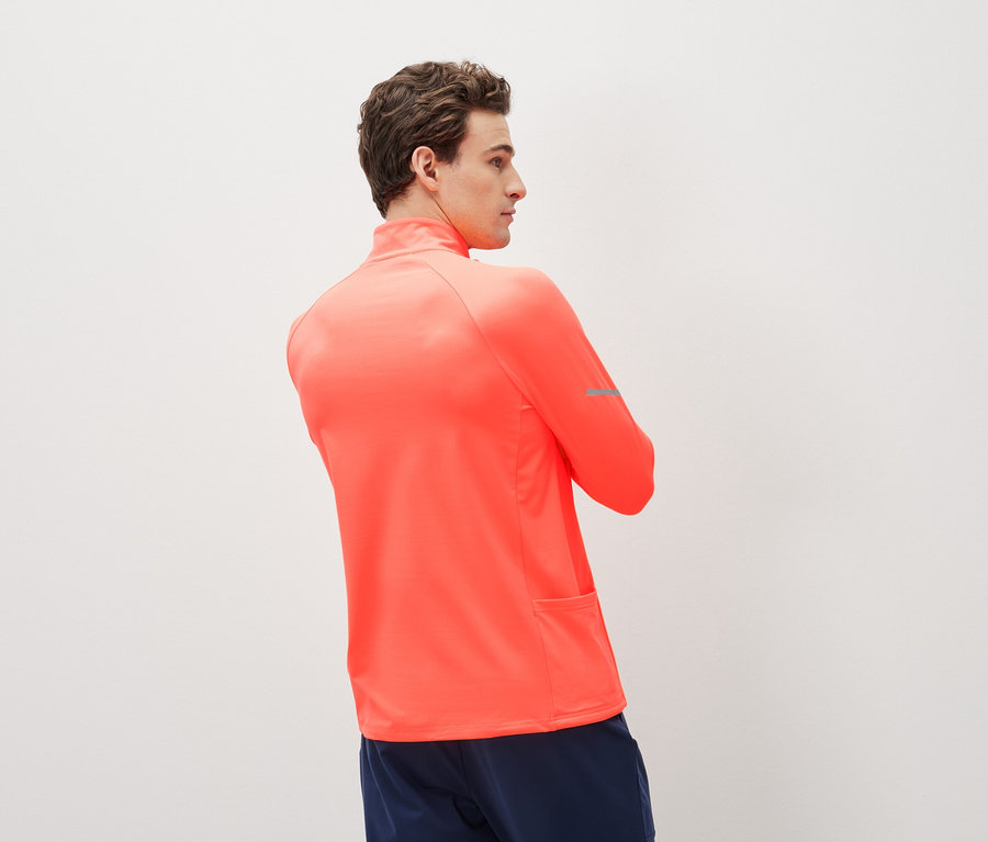 Muž v korálově červeném sportovním topu s dlouhým rukávem a tmavě modrých sportovních šortkách.